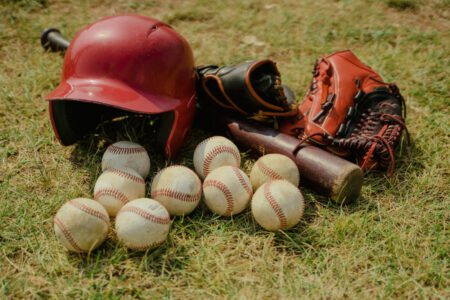 A collection of baseball gear including balls, a bat, helmet, and gloves on a grassy field.