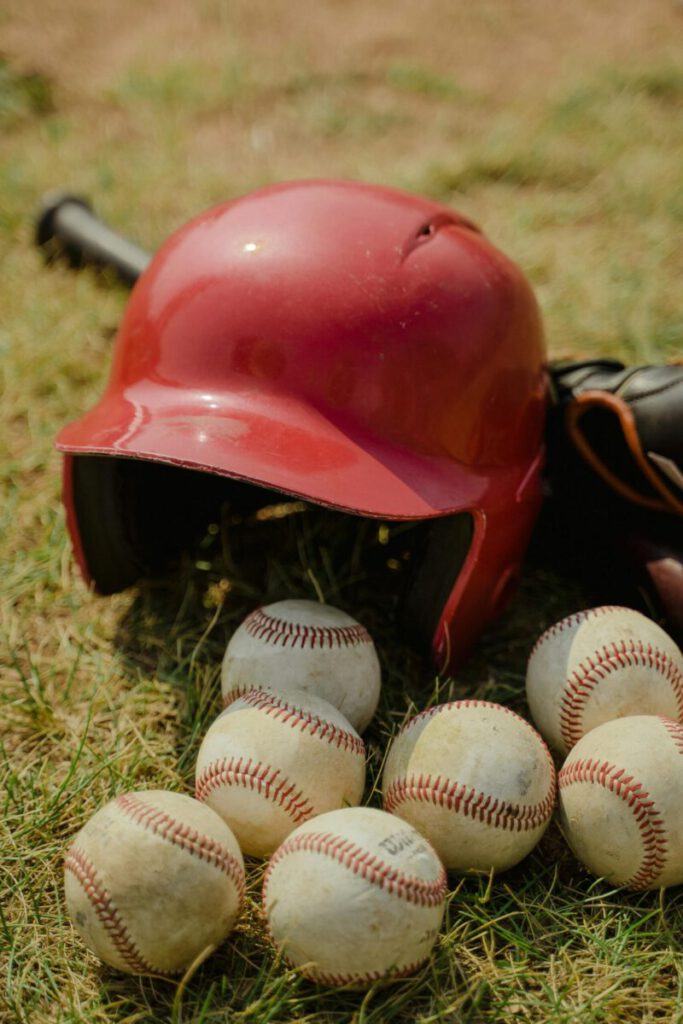 A red baseball helmet and multiple baseballs on a grass field, perfect for sports-themed designs.